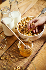 Kids hand holding bowl with healthy breakfast with flakes honey milk and honey dipper on old wooden table