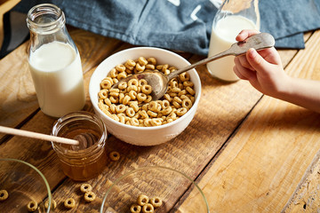 Kids hand holding bowl with healthy breakfast with flakes honey milk and honey dipper on old wooden table