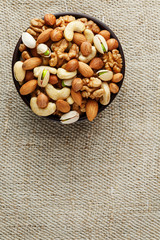 Mix of different nuts in a wooden cup against the background of fabric from burlap. Nuts as structure and background, macro. Top view.