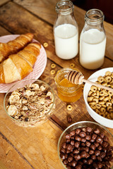 Healthy morning breakfast with different types of breakfast cereal with a spoon, honey croissants and milk on wooden table