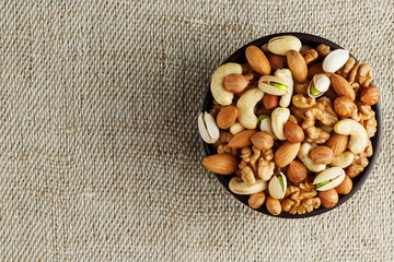 Mix of different nuts in a wooden cup against the background of fabric from burlap. Nuts as structure and background, macro. Top view.