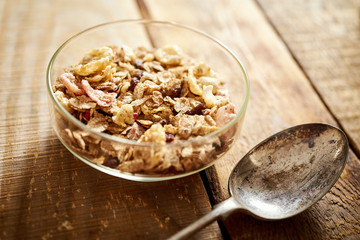 Healthy morning breakfast bowl full of organic granola with a rustic spoon on an old wooden table