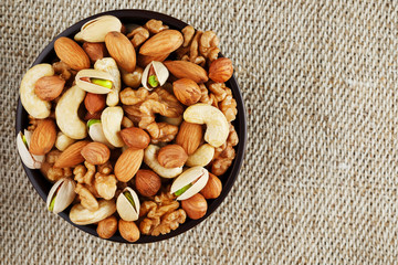 Mix of different nuts in a wooden cup against the background of fabric from burlap. Nuts as structure and background, macro. Top view.