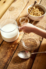 Kids hand holding bowl with healthy breakfast with flakes honey milk and honey dipper on old wooden table