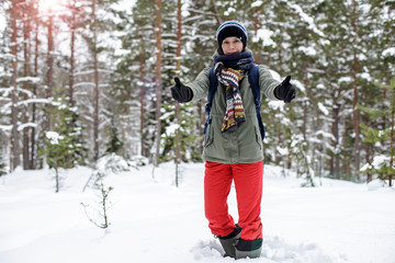 Fototapeta na wymiar A smiling woman in warm clothes stands stretching out her arms forward in a winter forest, against a background of pines and snowdrifts on a frosty day.
