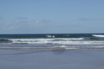surfer in the background in the middle of the waves on the beach