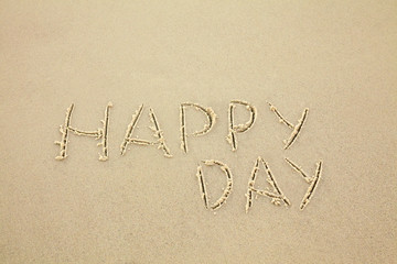 handwritten inscription happy day made in the sand, text on the beach