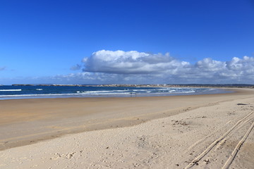 Sand in the foreground, blue sea and cloudy sky in the background