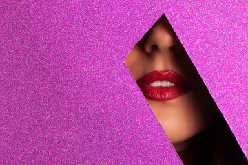 Girl with bright make up, red lipstick looking through hole in violet paper. Make up artist, beauty...