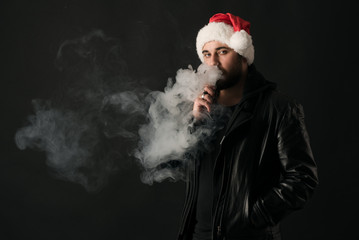 Man with beard in Santa red hat smoking electronic sigarette. vape pen. vape smoke. Christmas...