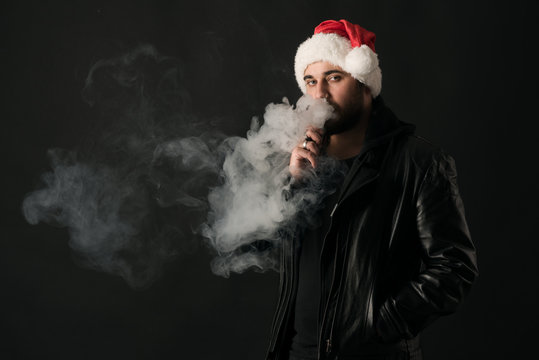 Man with beard in Santa red hat smoking electronic sigarette. vape pen. vape smoke. Christmas concept