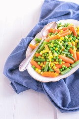 Erbsen, Möhren, grüne Bohnen und Mais liegen in einer weißen Schale