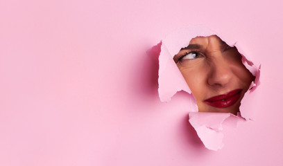 Portrait of displeased upset woman face. Discontent and unhappy girl through hole in pink paper...