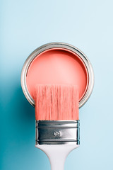 Brush with white handle on open can of Living Coral paint on blue pastel background. Color of the...