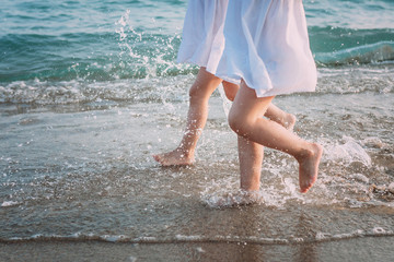 Two girls in white dresses run along the sea