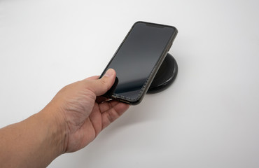 Hand holding mobile phone over black wireless charger isolated on white