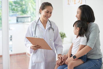 Male pediatrician reassuring mother of little Asian girl