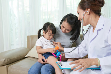 Little Vietnamese girl playing with plastic blocks when doctor listening to her heartbeat