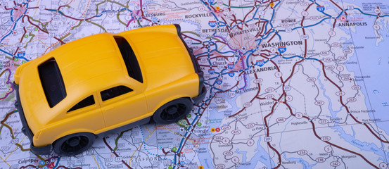 Yellow toy car on map surface (Washington, DC, USA). Road trip or rent car concept. Wide photo.