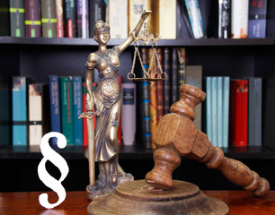 Justitia Figur mit Paragraphzeichen und Hammer auf einem Holztisch