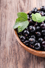 Half of big wooden bowl with fresh black currant on wooden background close-up top view.