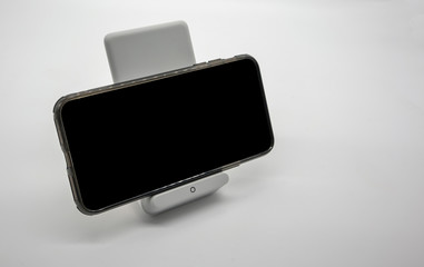 Black cellphone charging on modern designed wireless charger stand isolated on white.