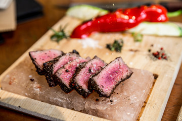 Juicy medium Beef Rib Eye steak slices in pan on Himalayan pink salt plates.