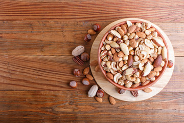 Mixed different kinds of nuts in ceramic bowl on brown wooden background with copy space.