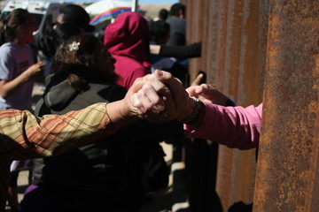personas se saludan entre el muro que divide mexico de estados unidos