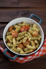 Bowl of fusilli served with basil pesto sauce and cherry tomatoes, vertical shot on a rustic wooden background