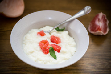 sweet boiled semolina porridge in a plate with slices of red grapefruit