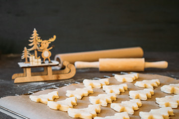 Raw dough cookies in Christmas tree shape ready to bake. Christmas Gingerbread cookies with baking paper on the tray on the dark background with wooden rolling pin and deer