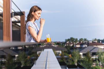 Profile of cheerful lady is holding glass of orange juice and looking ahead with smile. Copy space...