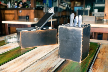 Flatware, cutlery, silverware in wooden box and Paper napkins, pepper and salt shaker on the table. Restaurant interior, pub, cafe background
