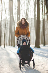 Fototapeta na wymiar Portrait of young brunette woman with her son in the stroller walking in the park on beautiful winter day.