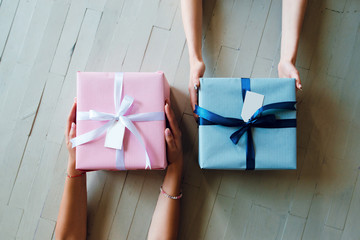 Top view of women hands holding gift boxes. Pink and blue present boxes on the wooden background.