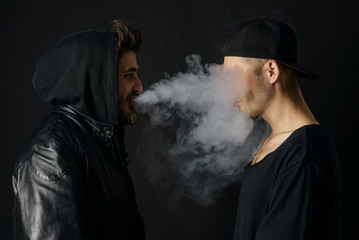 Bad habit, smoking in a public place. Two Young man blowing smoke to join it in one cloud at black...