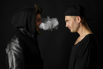 Bad habit, smoking in a public place. Two Young man blowing smoke to join it in one cloud at black...