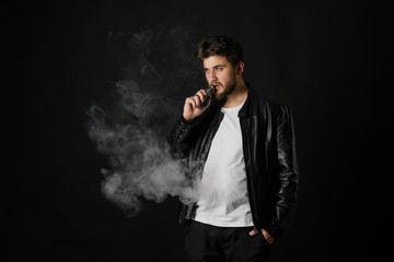 Man with vaping mod exhaling steam at black studio background. Bearded guy smoking e-cigarette to...
