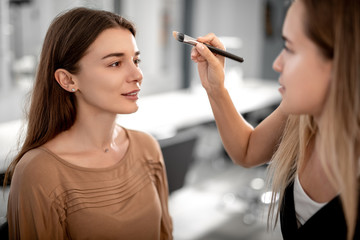 Visagiste is using special brush and doing foundation for smiling pretty woman