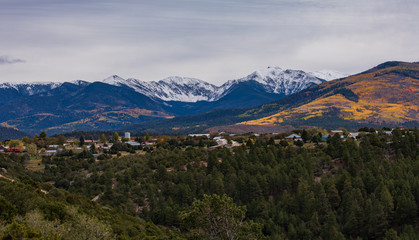 Fototapeta na wymiar Small town at the foot of mountains with snow cap tops and autumn forest