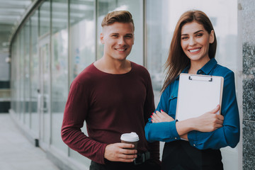 Concept of friendly relationship on work. Waist up portrait of young cheerful man and stylish woman staying on street