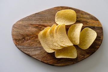 Bunch of salty crisps presented on a wooden board, grey background