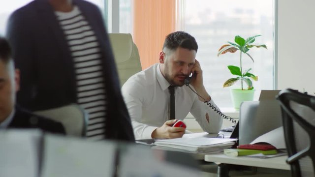 Stressed middle-aged Caucasian man sitting at office desk and arguing with someone on the phone