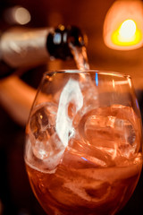 Barman pouring fresh alcoholic drink into the glasses with ice cubes on the bar counter