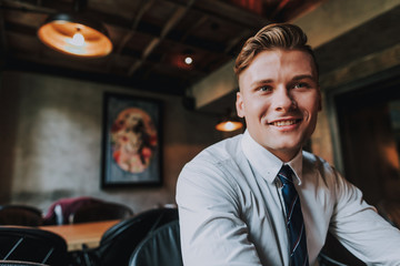 Concept of success and positive mind. Waist up portrait of handsome smiling businessman having lunch in cafe. Copy space on left