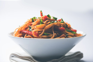 Schezwan Noodles or vegetable Hakka Noodles or chow mein is a popular Indo-Chinese recipes, served in a bowl or plate with wooden chopsticks. selective focus