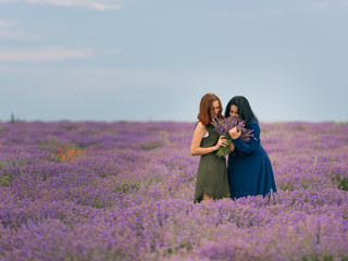 Two young girls with different hair color in blue and green dresses, posing together in a lavender field.