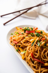 Schezwan Noodles or vegetable Hakka Noodles or chow mein is a popular Indo-Chinese recipes, served in a bowl or plate with wooden chopsticks. selective focus