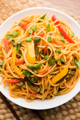 Schezwan Noodles or vegetable Hakka Noodles or chow mein is a popular Indo-Chinese recipes, served in a bowl or plate with wooden chopsticks. selective focus